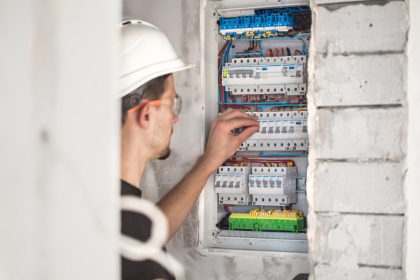 Man, an electrical technician working in a switchboard with fuses. Installation and connection of electrical equipment. Man, an electrical technician working in a switchboard with fuses. Installation and connection of electrical equipment. Professional with tools in hand. concept of complex work, space for text.